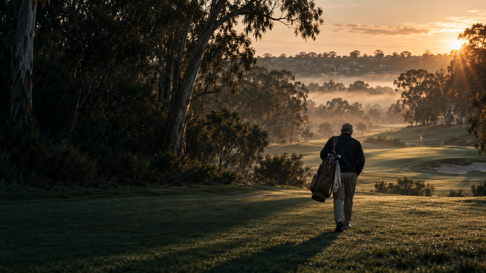 A golfer walking toward a green in the early morning